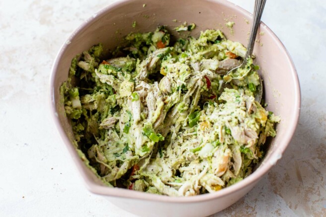Stirring together mashed avocado with chicken and other salad ingredients.