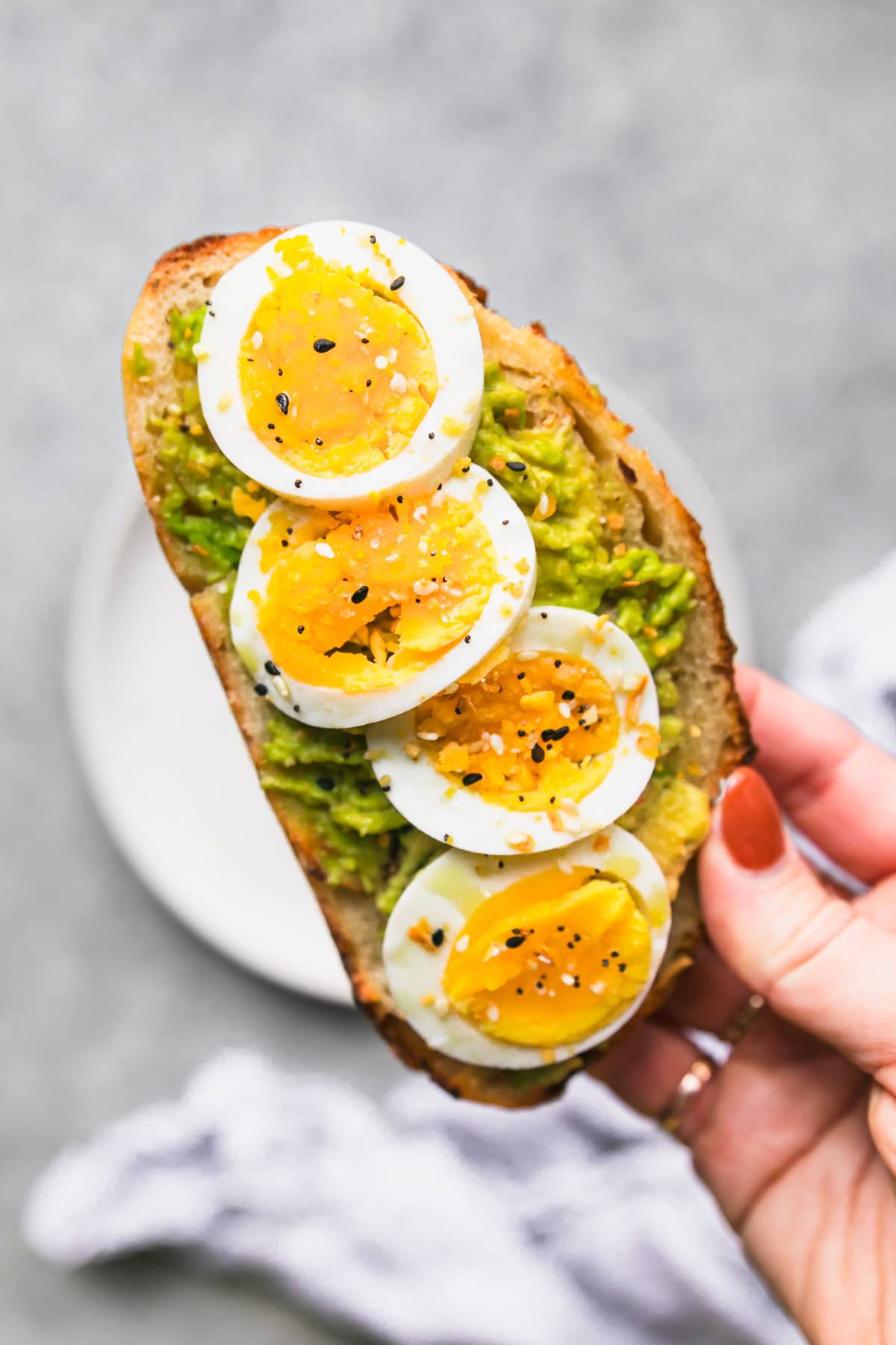 Hand holding avocado toast with sliced hard-boiled egg.