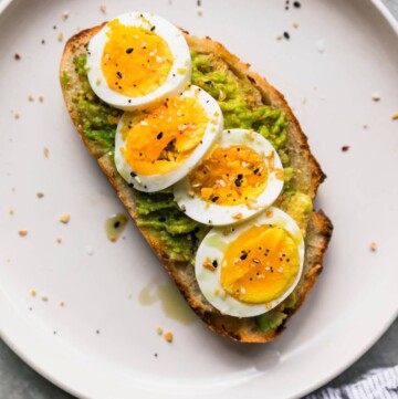 Avocado toast with hard boiled egg on a white plate.