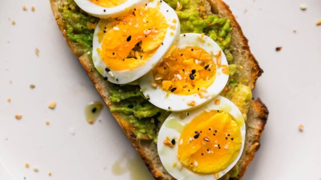 Avocado toast with hard boiled egg on a white plate.