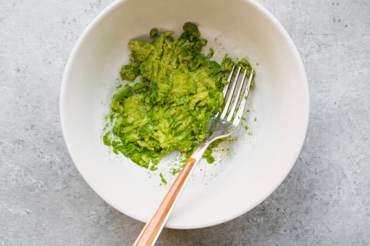 Using a fork to mash avocado in a white bowl.