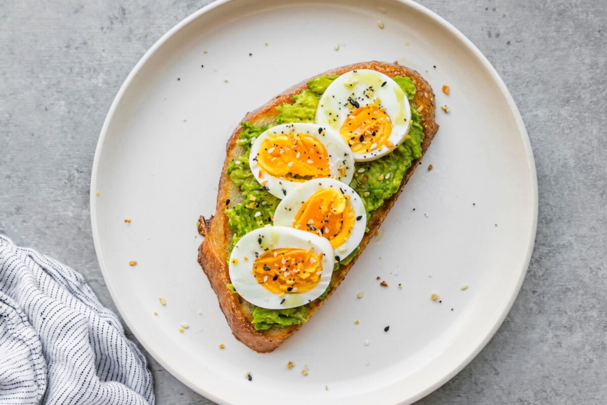 Piece of toast topped with mashed avocado and slices of hard-boiled egg on a white plate.