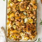 Chicken and potatoes in a glass baking dish near fresh rosemary.
