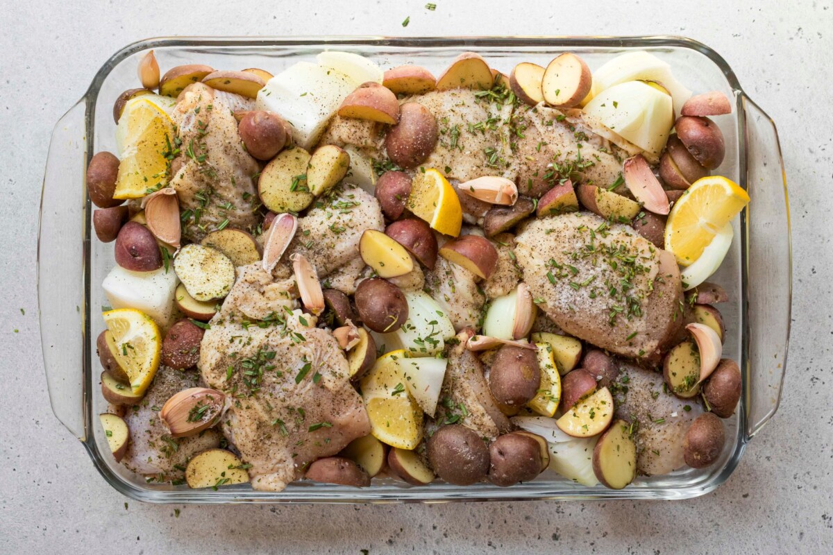 Seasoned chicken and potatoes in a glass dish before being baked.