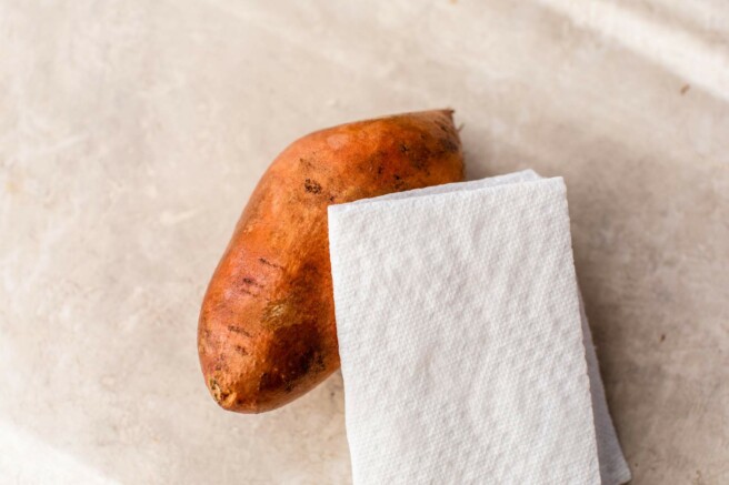 Patting a sweet potato dry with a paper towel.