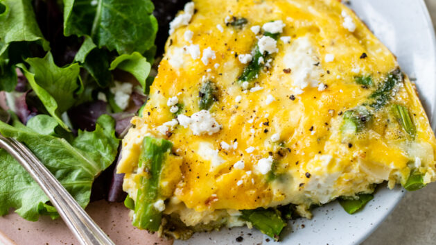 Slice of asparagus frittata on a white plate with a salad.