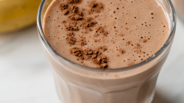 banana pbfit chocolate protein shake in a glass next to a banana