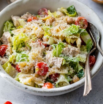 Chicken caesar pasta salad served in a small white bowl with a fork and spoon.
