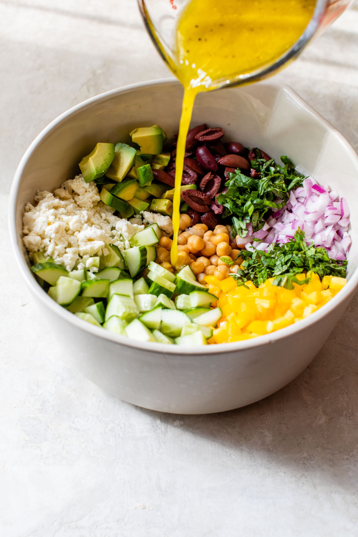 greek salad dressing pouring over top of a mediterranean chickpea salad