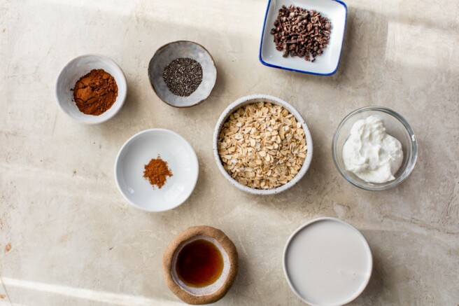 Oats, cocoa powder, chia seeds, greek yogurt and maple syrup divided into small bowls.
