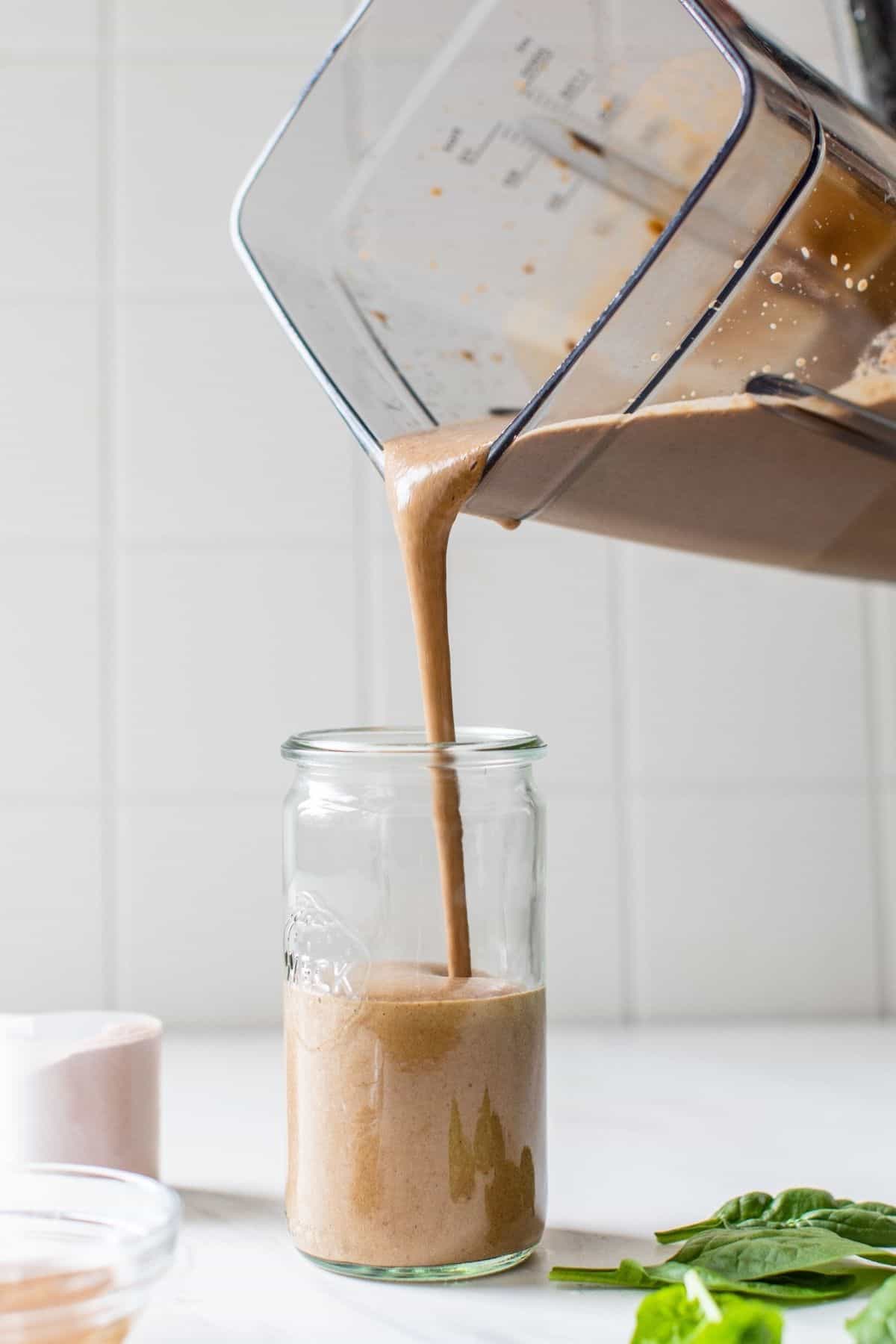pouring a chocolate protein shake out of a blender and into a glass