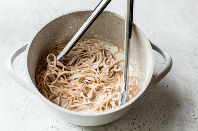 Tossing noodles with sauce in a large pot.