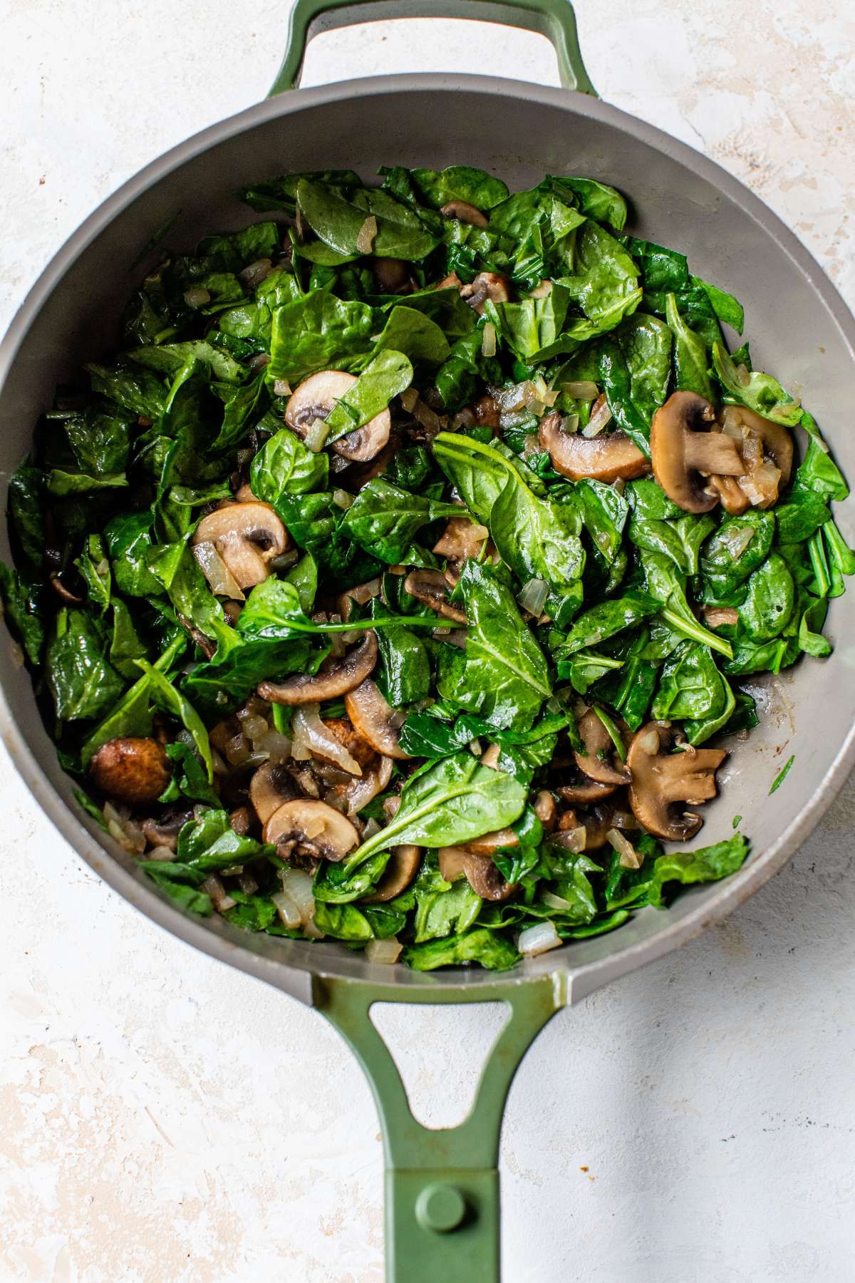 Sautéing spinach with mushrooms in a large skillet.