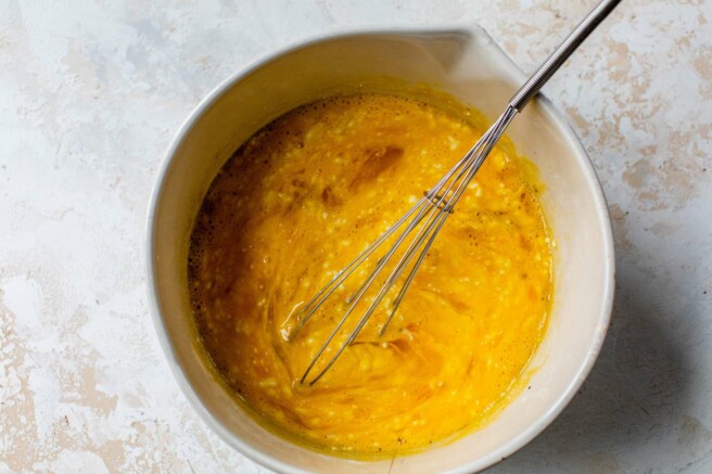 Whisking eggs with cottage cheese in a large bowl.