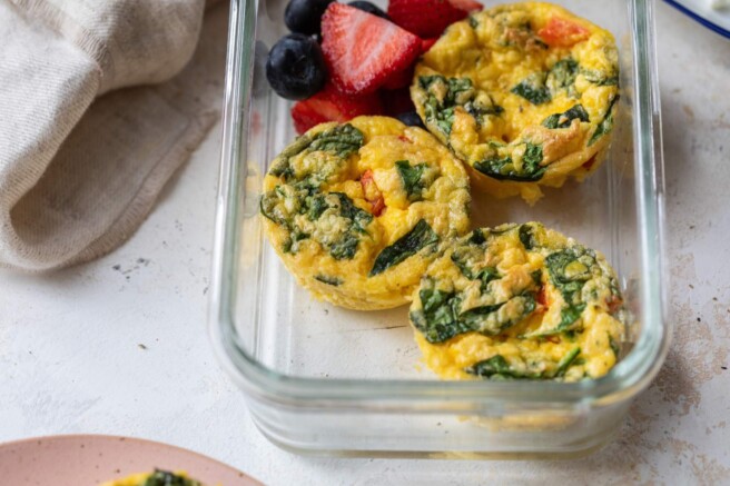 Egg bites in a glass storage container with fresh berries.