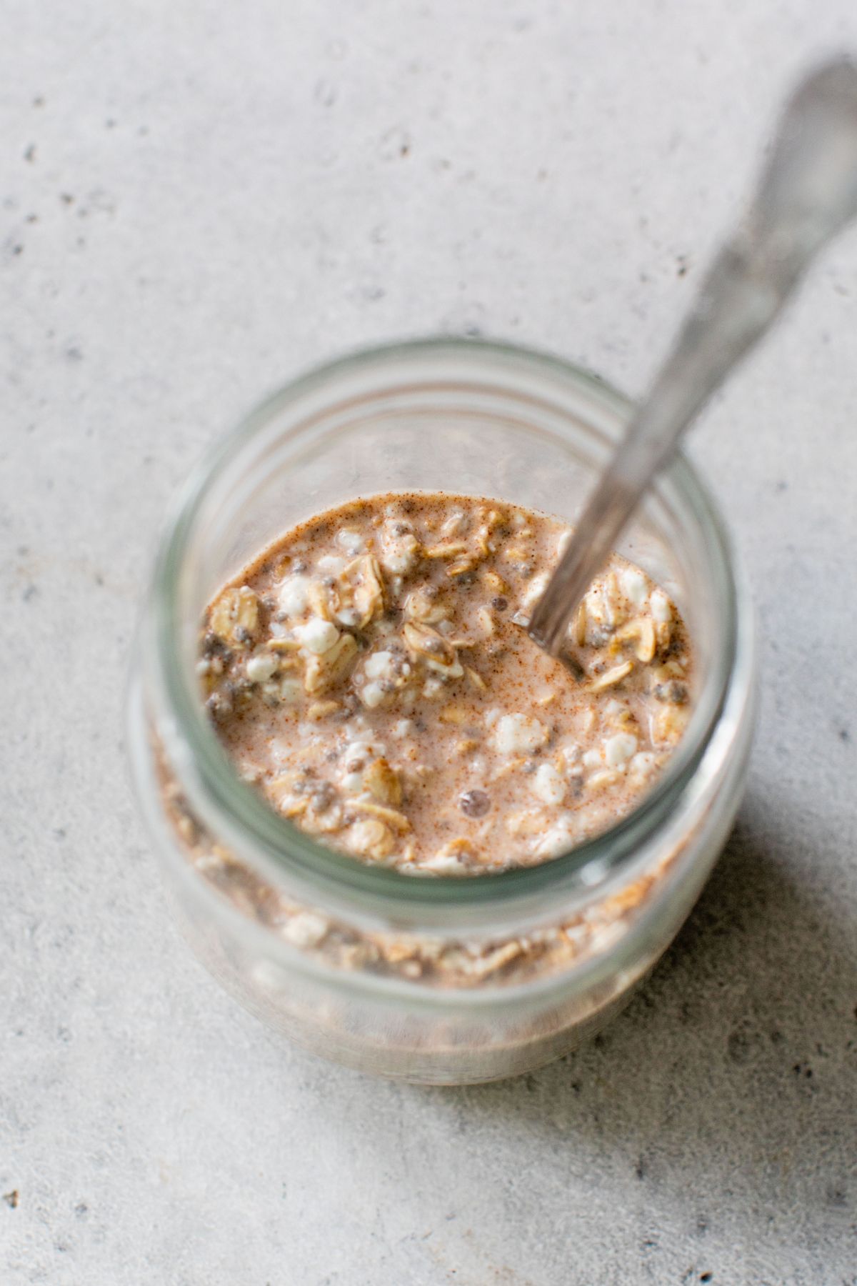 Stirring oats with cottage cheese, milk and cinnamon in small jar.