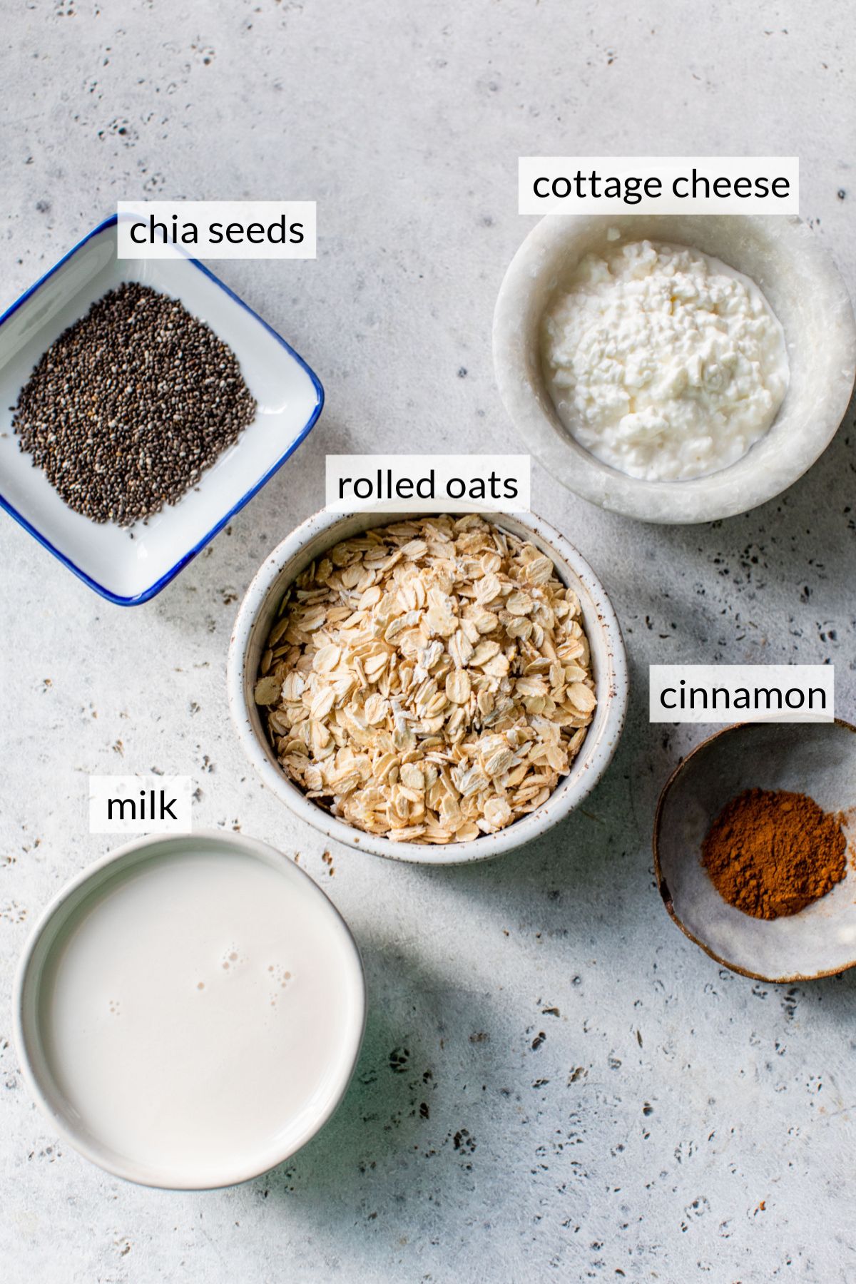 Small bowls with chia seeds, cottage cheese, oats, milk and cinnamon.