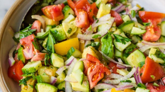 Cucumber tomato salad with avocado and red onion served in a white bowl with a spoon.
