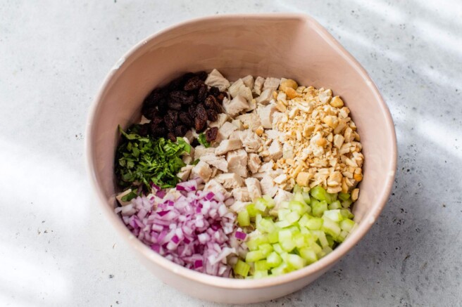 Chicken, red onion, cashews, herbs and raisins in a bowl.