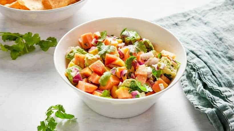 papaya salsa in a white bowl served with tortilla chips
