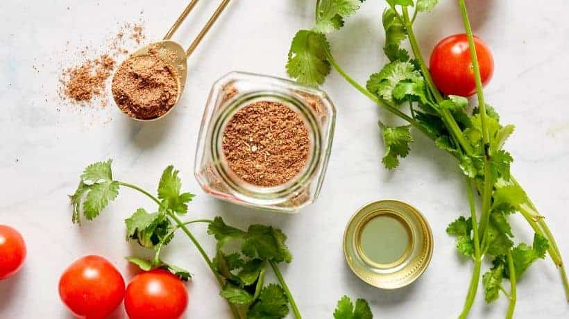 taco seasoning in a glass jar near tomatoes and cilantro