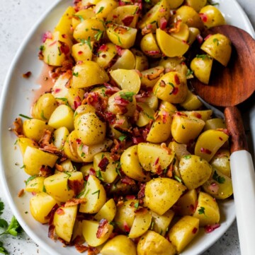 German potato salad served on a large white platter with a wooden serving spoon.