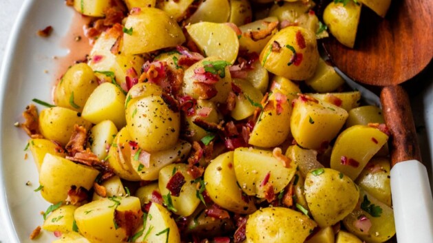 German potato salad served on a large white platter with a wooden serving spoon.
