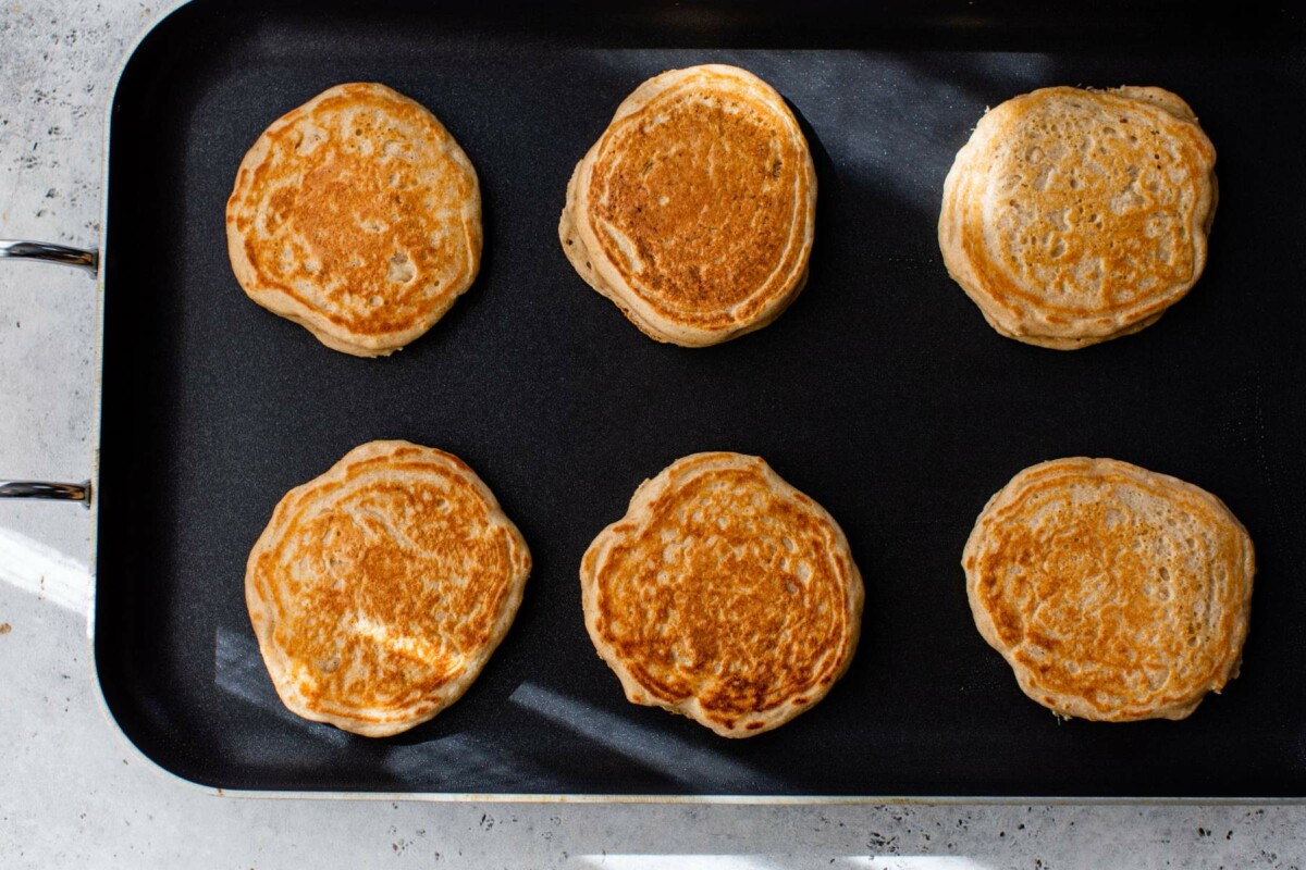 Greek yogurt pancakes cooking on a griddle.