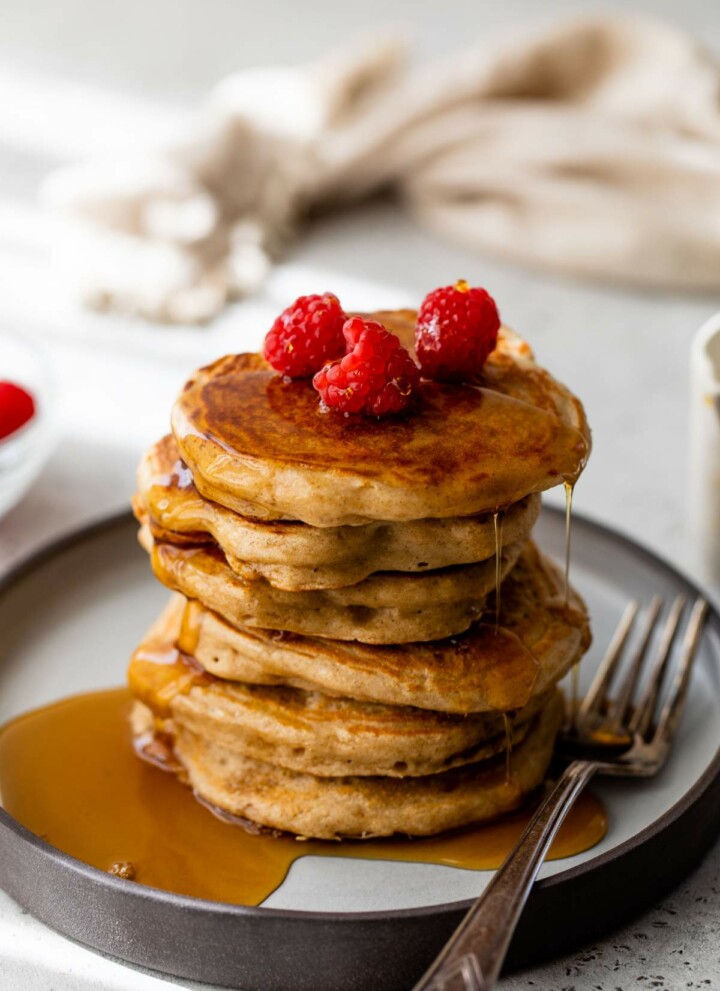 Stack of Greek yogurt pancakes topped with maple syrup and raspberries.