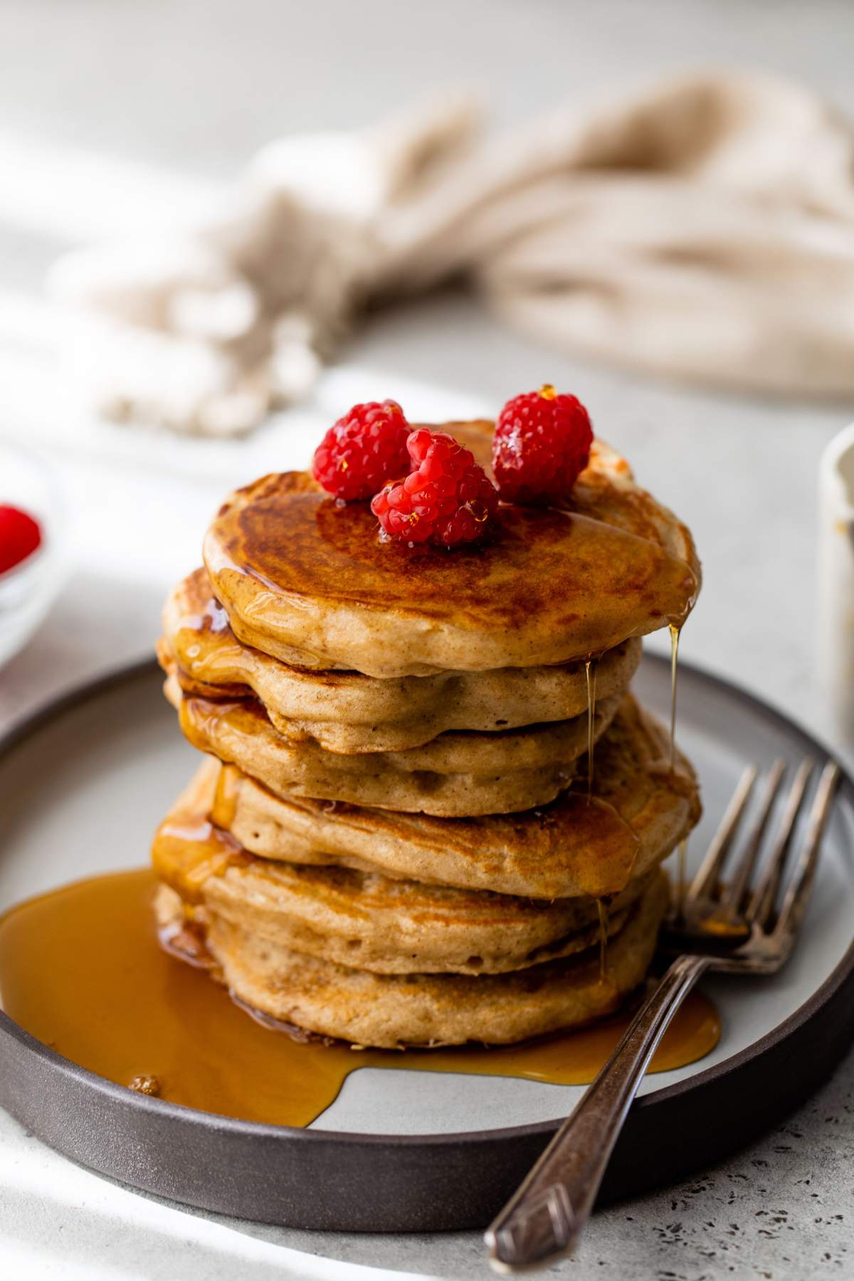 Stack of Greek yogurt pancakes topped with maple syrup and raspberries.