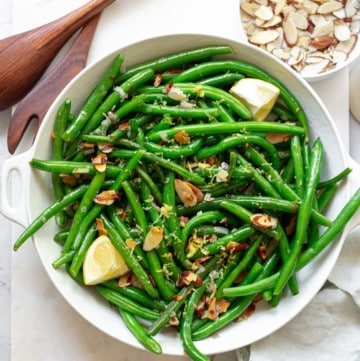 green bean almandine in a large white bowl near a small bowl of almonds