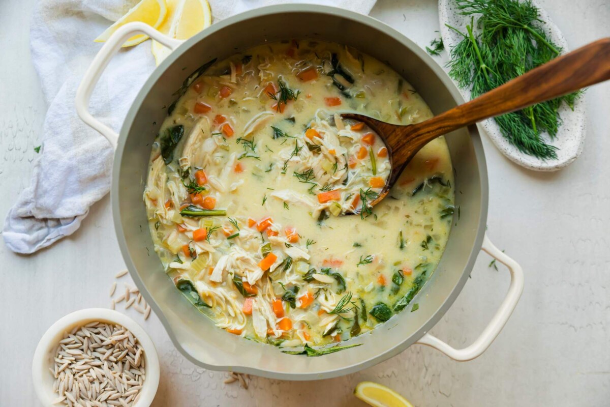 Lemon chicken soup with orzo in a large soup pot with a wooden spoon.