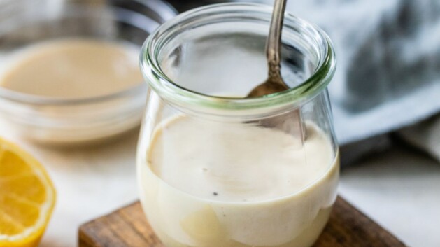 Small jar of lemon tahini dressing with a spoon inside.