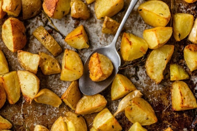 serving oven roasted potatoes off of a baking sheet with a spoon