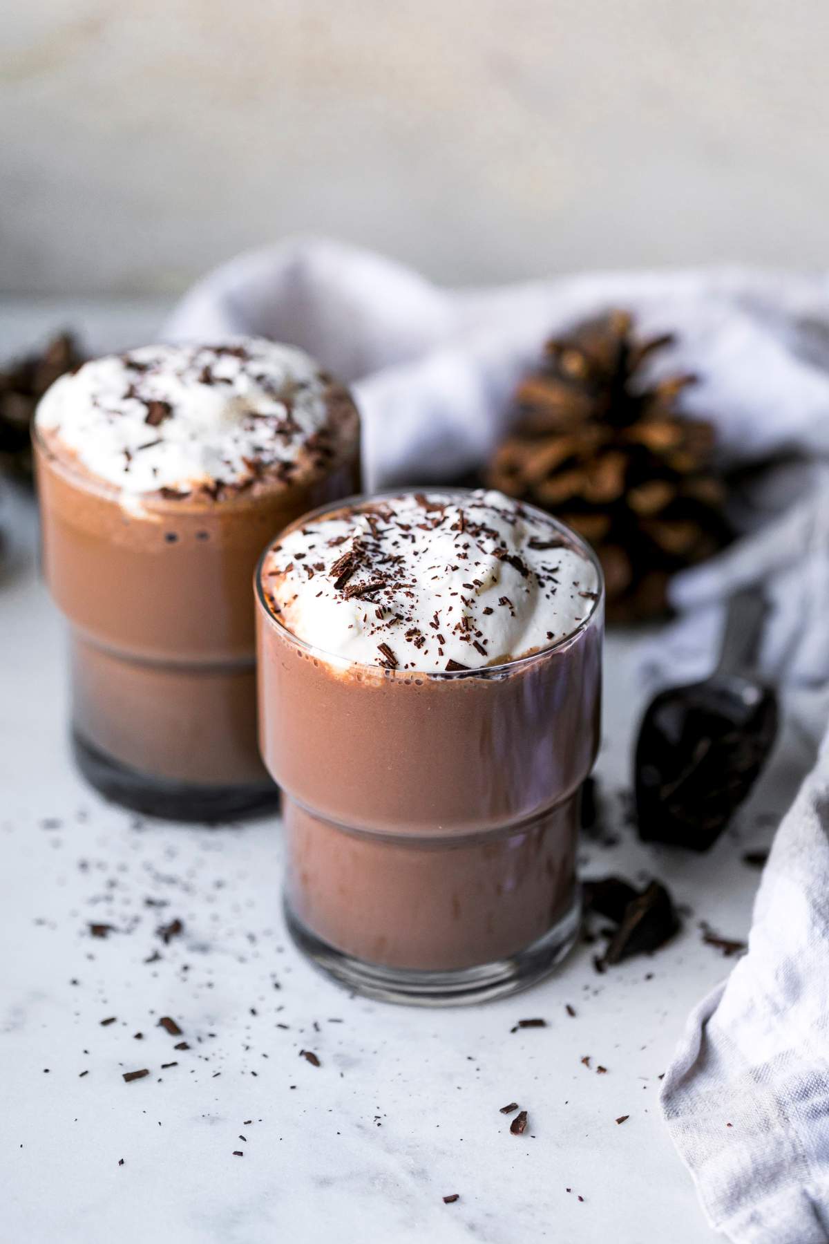 Two small glasses of protein hot chocolate topped with whipped cream and chocolate shavings.