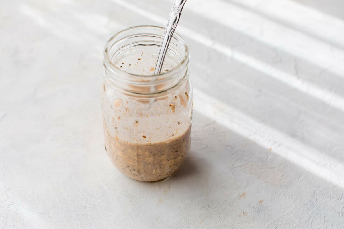 Stirring milk and Greek yogurt with rolled oats and protein powder in a mason jar.