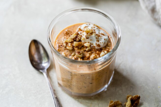 Pumpkin overnight oats in a glass jar topped with nuts and yogurt.