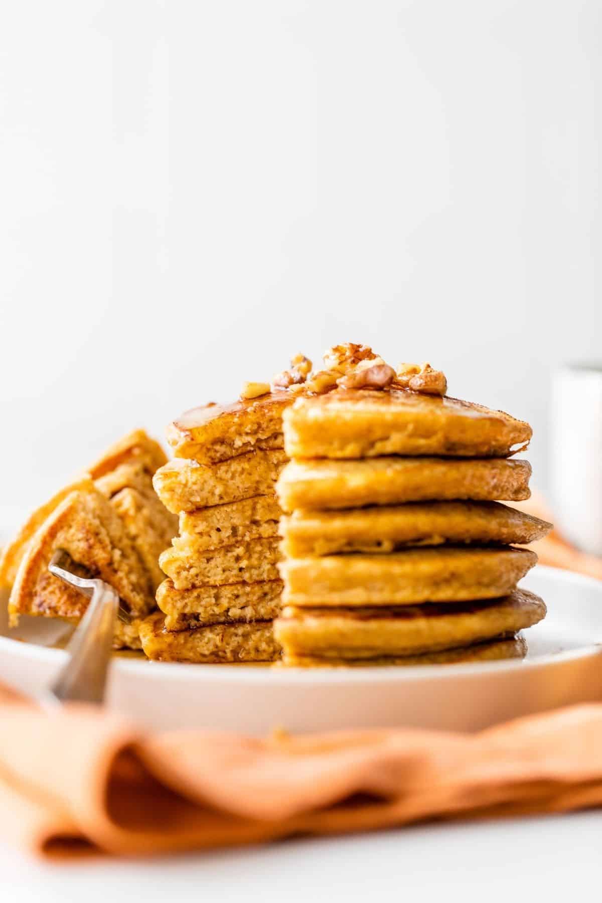 stack of pumpkin protein pancakes with maple syrup and chopped nuts