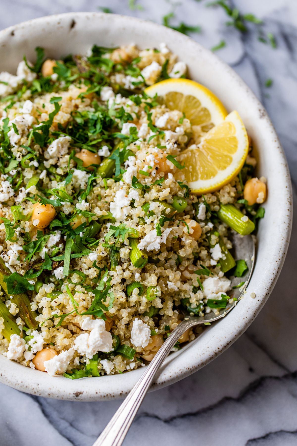 Quinoa mixed with asparagus, chickpeas, feta and fresh herbs in a white bowl.