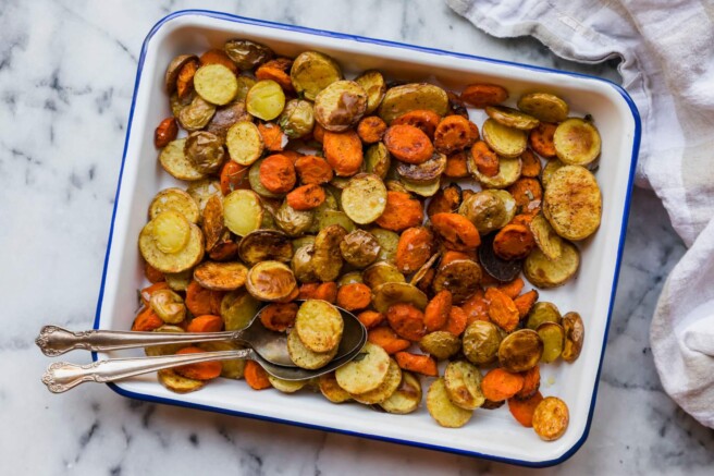 Roasted carrots and baby potatoes on a serving tray with a serving spoon.