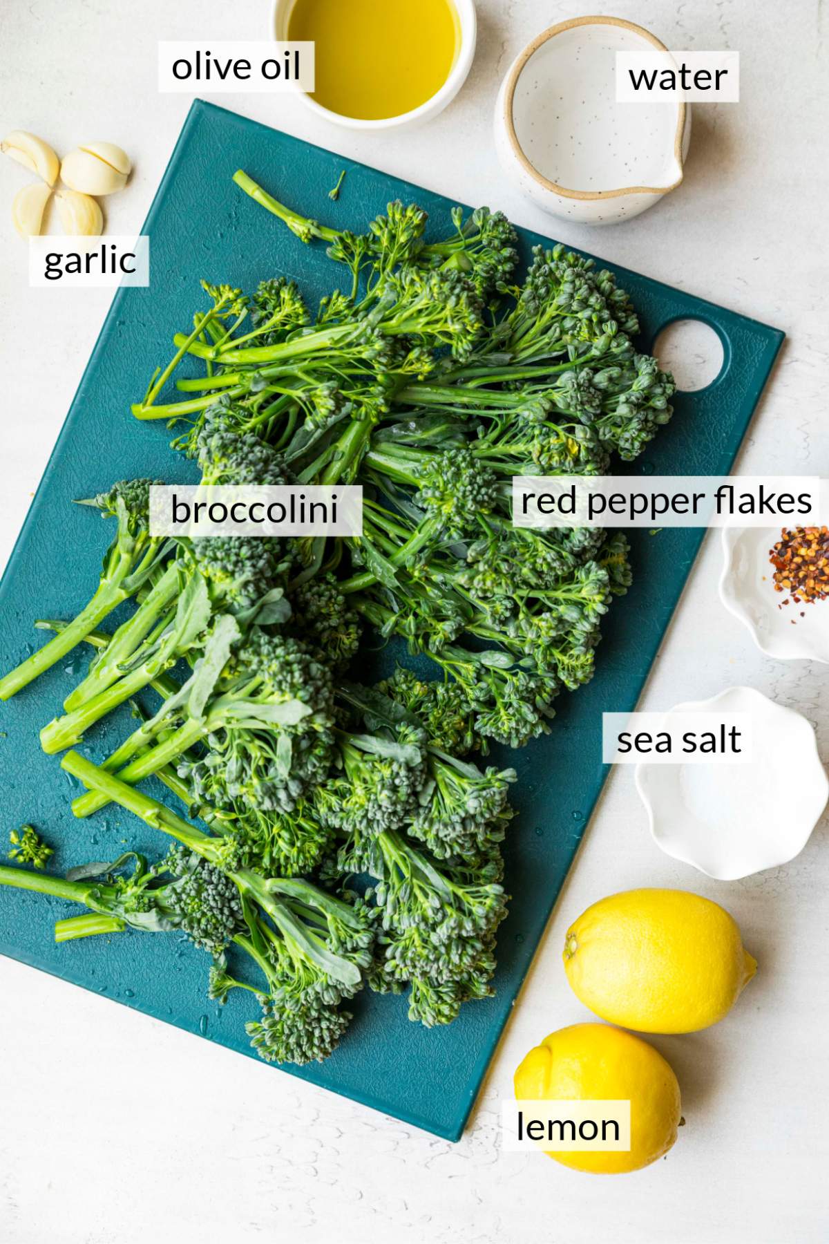Broccolini on a cutting board near lemons, salt, red pepper flakes and garlic.