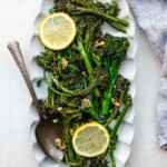 Sautéed broccolini served on a white plate with fresh lemon slices.