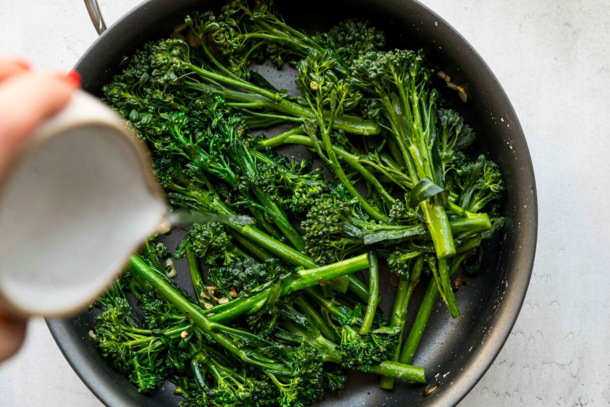 Pouring water into a pan with broccolini.