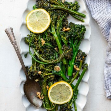 Sautéed broccolini served on a white plate with fresh lemon slices.