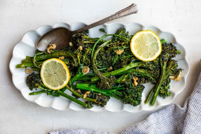 Sautéed broccolini on a white serving plate with slices of lemon.