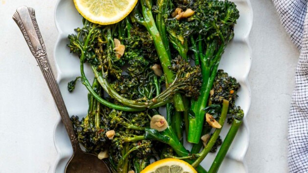 Sautéed broccolini served on a white plate with fresh lemon slices.