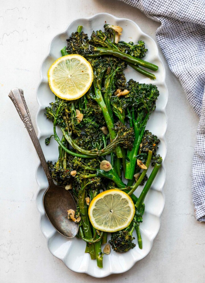 Sautéed broccolini served on a white plate with fresh lemon slices.