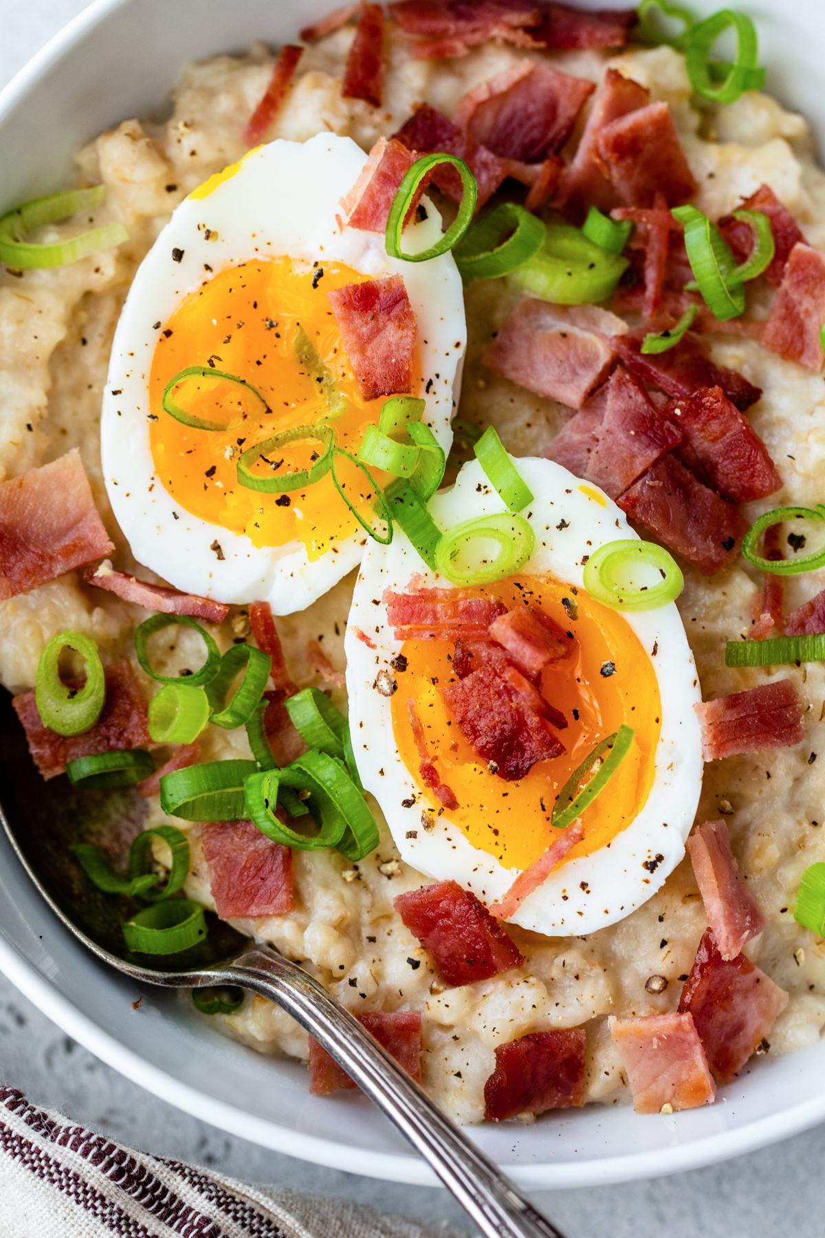 a close up photo of hard boiled eggs an crumbled turkey bacon over savory rolled oatmeal