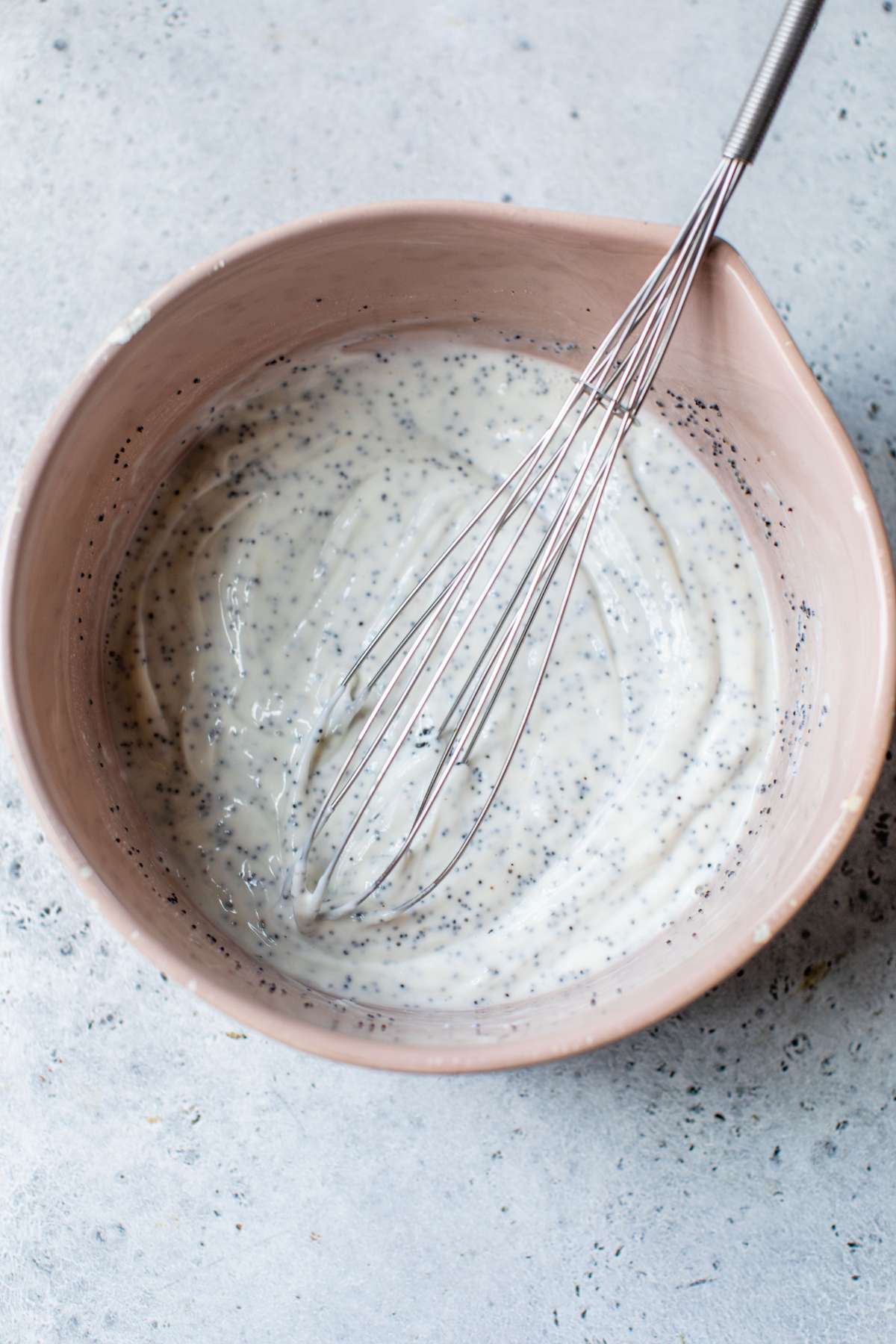 Whisking Greek yogurt with poppy seeds, honey and apple cider vinegar in a large bowl.