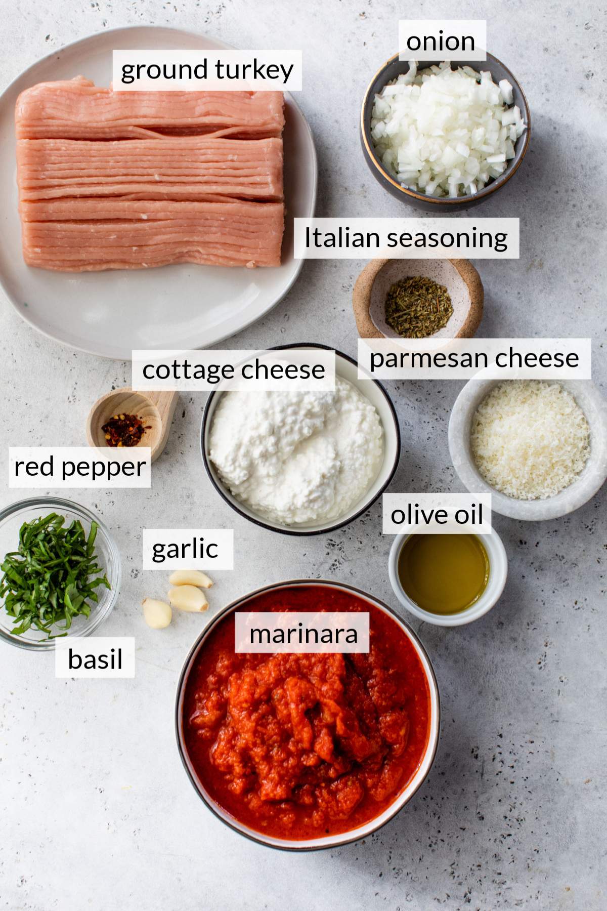Ground turkey on a plate near cottage cheese, marinara, parmesan cheese and other ingredients in small bowls.